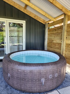 A hot tub with a wicker exterior, a glass door, and a wooden ceiling. - The Pigsty at the Secret Garden (Ashford)