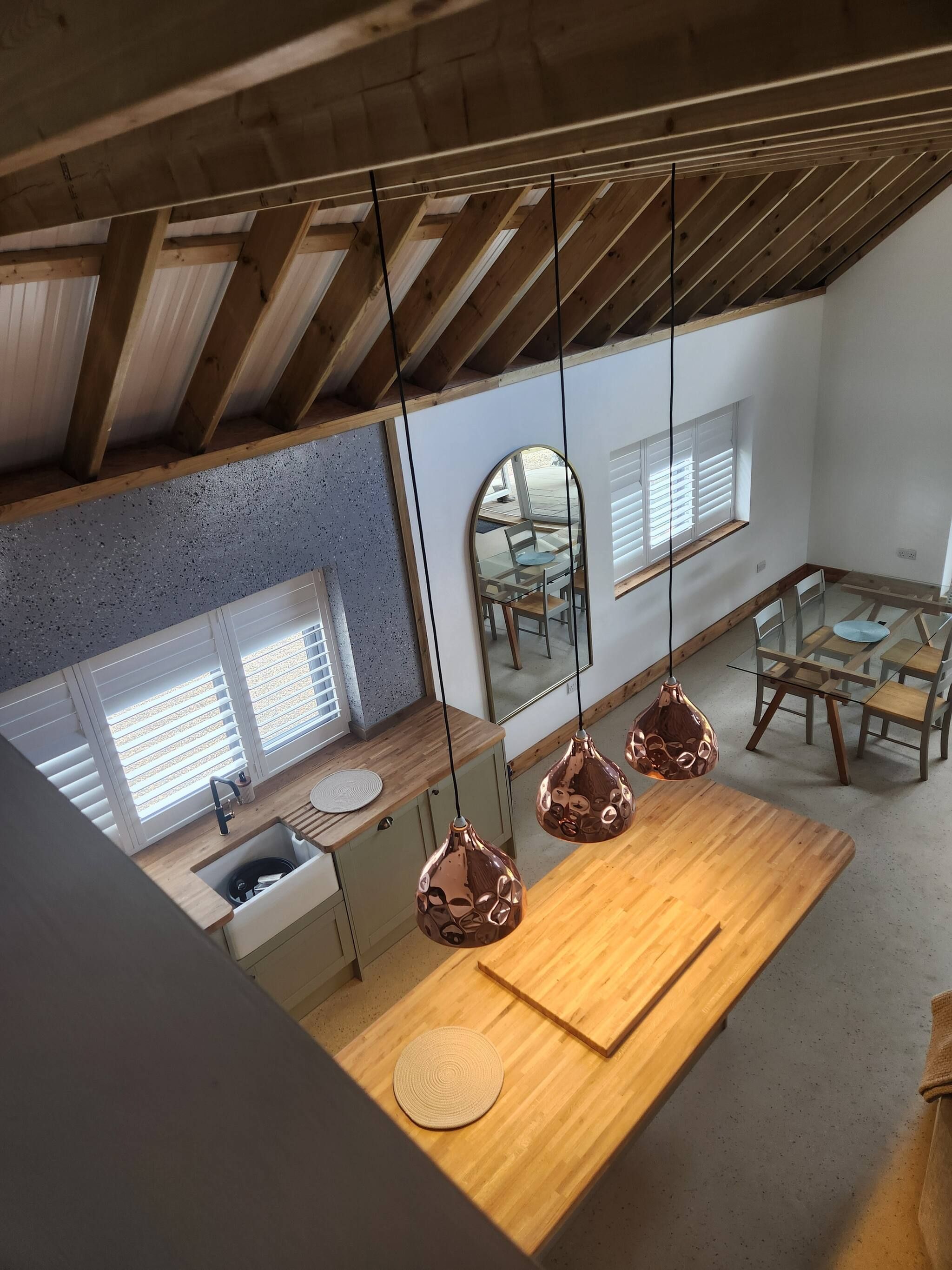 Een moderne keuken met een houten aanrecht, een spoelbak en een ronde mat. Er is een eethoek met een tafel en stoelen, en een grote spiegel aan de muur.