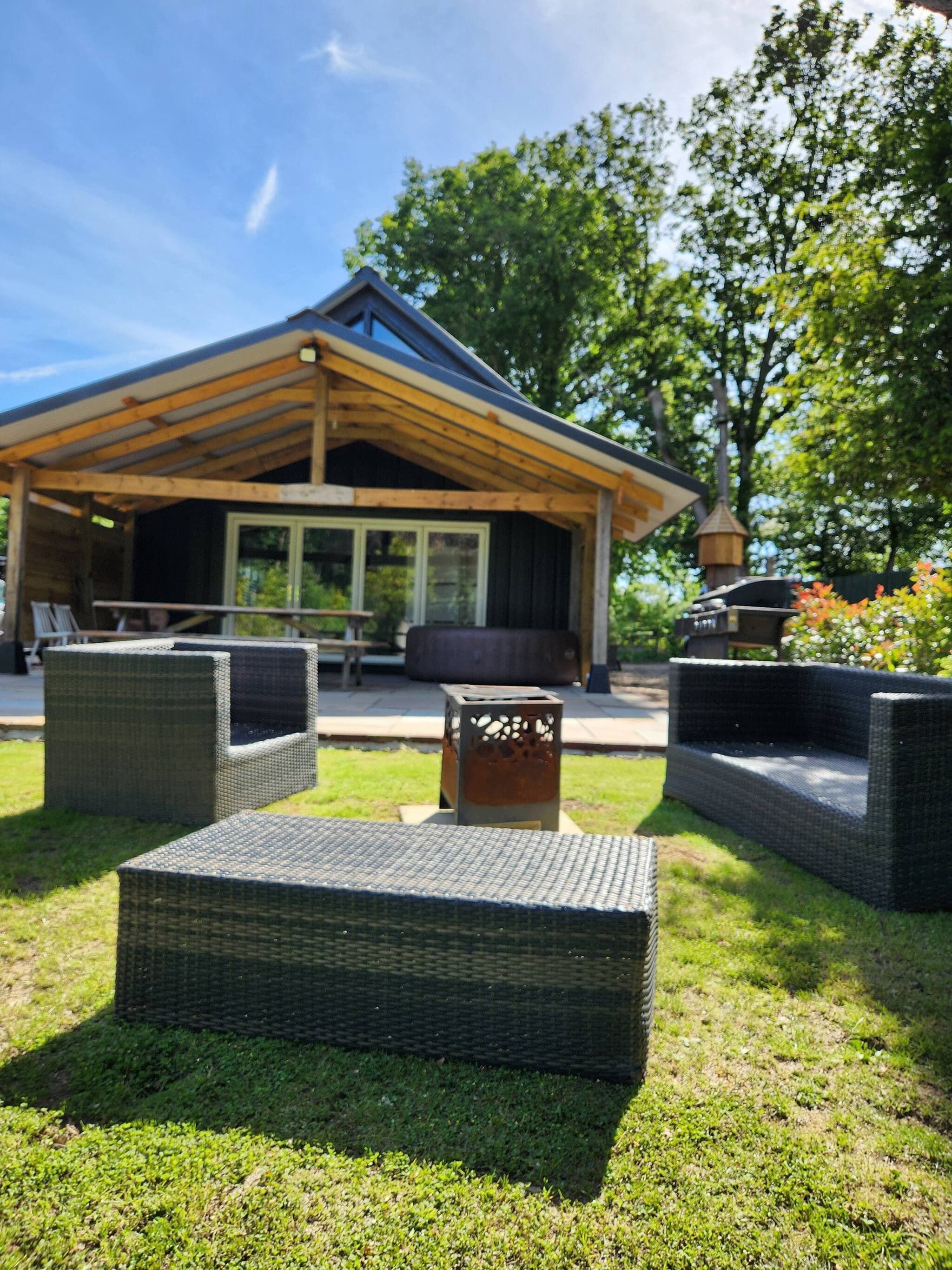 A modern outdoor seating area with wicker furniture, a wooden pergola, and a view of a building with large windows.