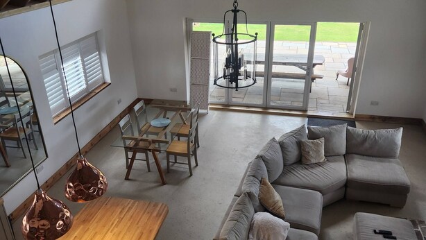 A spacious living area with a large sectional sofa, a wooden dining table, and a hanging light fixture. - The Pigsty at the Secret Garden (Ashford)