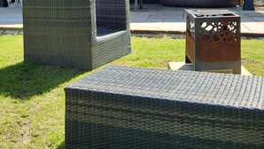 A covered outdoor seating area with wicker furniture and a metal table. - The Pigsty at the Secret Garden (Ashford)