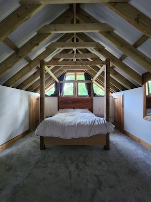A bedroom with a wooden ceiling, a large bed, and a window. - The Pigsty at the Secret Garden (Ashford)