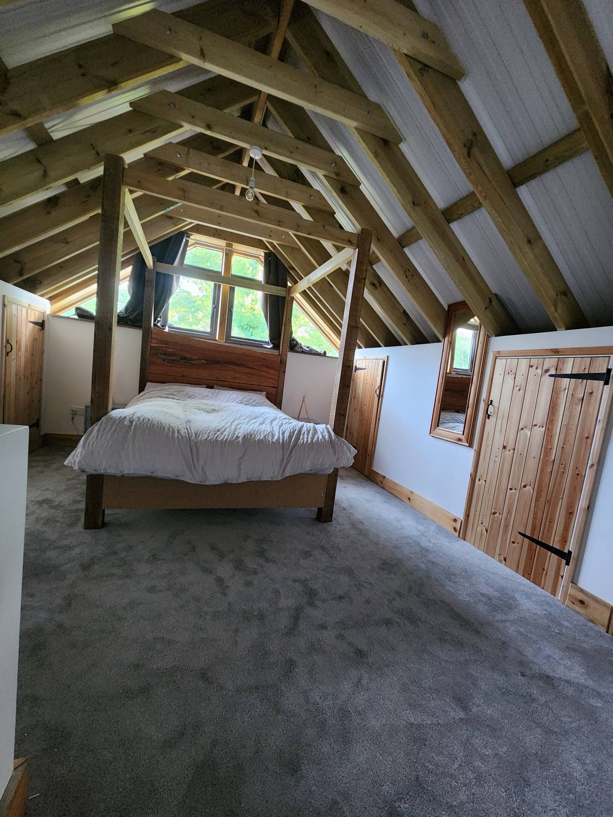 Une chambre avec un plafond en bois, un lit, une fenêtre et une armoire.