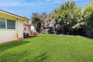Ein Wohnhaus mit gepflegtem Rasen, einer Terrasse und verschiedenen Bäumen und Sträuchern.