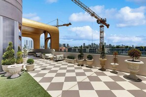 A rooftop terrace with a checkered floor, potted plants, outdoor furniture, and a view of the city skyline. - NoMad #628 - Private Balcony (Miami)