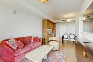 A modern living room with a red sofa, a wooden cabinet, a dining area with a table and chairs, and a kitchen in the background. - NoMad #628 - Private Balcony (Miami)