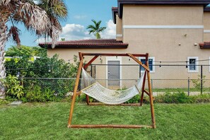A hammock swing in a backyard with a house in the background. - The Palms Unit 1 - Enclosed Yard (Fort Lauderdale)