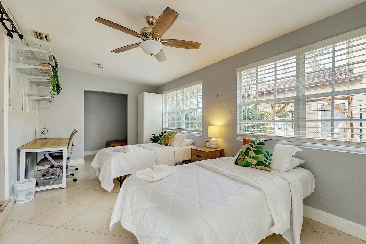 A room with two beds, a desk, and a ceiling fan.
