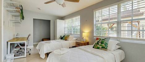 A room with two beds, a desk, and a ceiling fan.