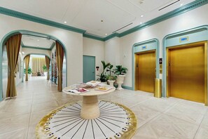 A hotel lobby with a round table, two elevators, and a corridor leading to a reception area. - NoMad #415 - Private Balcony (Miami)