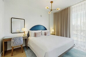A hotel room with a large bed, a desk with a chair, a mirror, and a window with curtains. - NoMad #415 - Private Balcony (Miami)