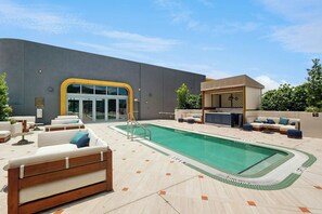 A pool area with a lounge chair, a covered seating area, and a building with a glass entrance. - NoMad #415 - Private Balcony (Miami)