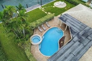 Ein Schwimmbecken mit Whirlpool, umgeben von einer Terrasse mit Liegestühlen, einer überdachten Sitzgelegenheit und Blick auf das Wasser.