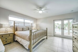 Ein Schlafzimmer mit einem Bett, Nachttischen, einem Deckenventilator und Blick durch eine Glastür auf einen Außenbereich.