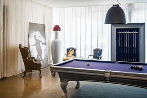 A billiards table with a pool cue rack, a chair, and a vase with red flowers. - Tony Ultimate Experience Miami (Miami)