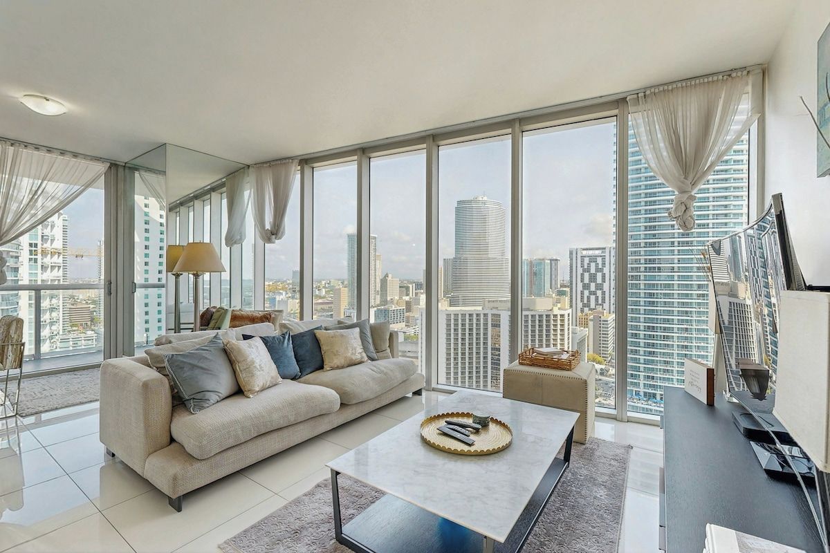 Ein modernes Wohnzimmer mit großem Fenster, einer Couch, einem Couchtisch und Blick auf die Stadt.