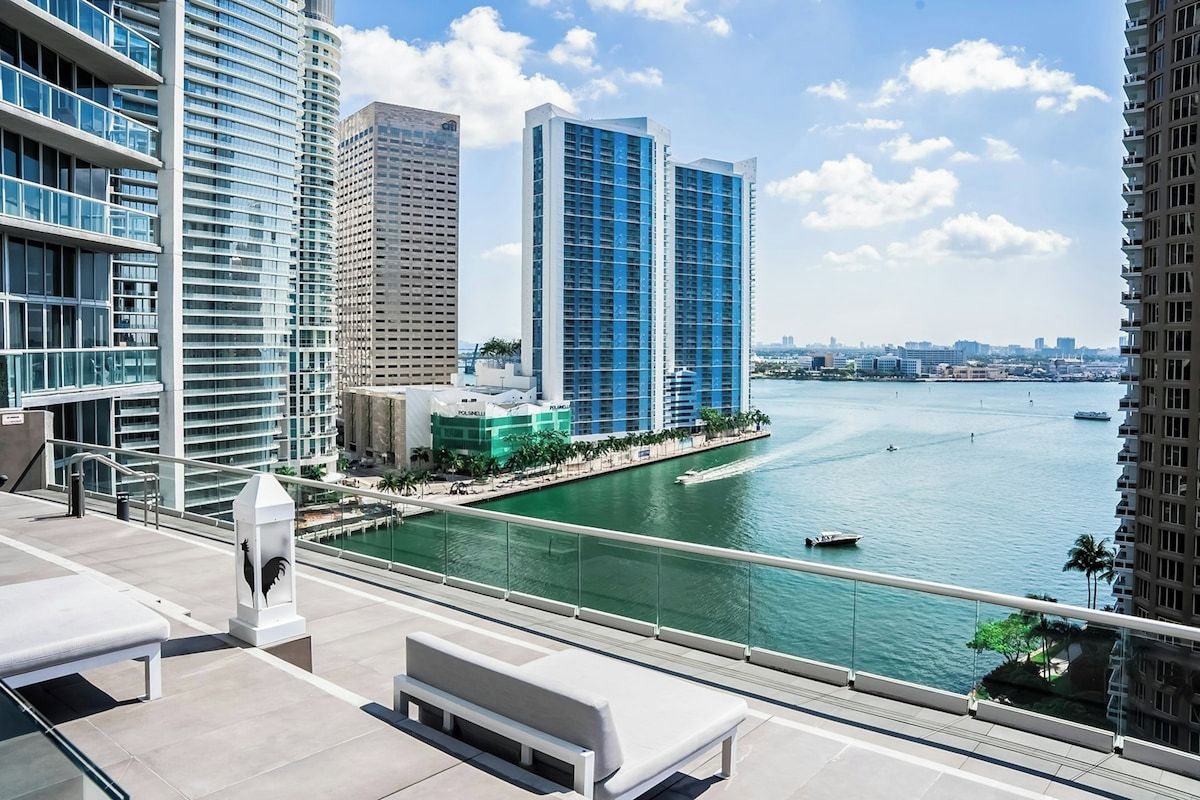 A high-rise building with a view of a river and other buildings in the background.