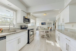 A modern kitchen with white cabinetry, a built-in oven, a microwave, and a dining area with a table and chairs. - Pompano Beach Getaway (Pompano Beach)
