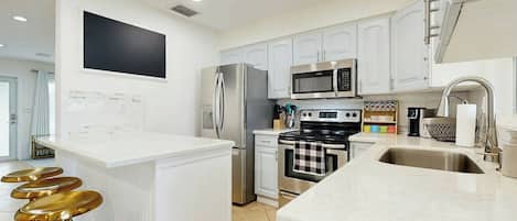 A modern kitchen with white cabinets, stainless steel appliances, and a marble countertop.