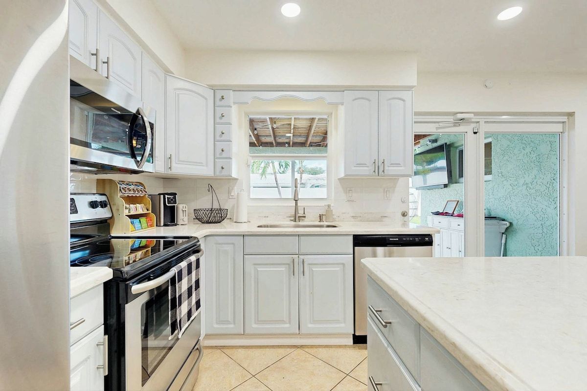 A modern kitchen with white cabinetry, a built-in oven, a dishwasher, and a window above the sink.