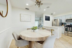 A modern kitchen with white cabinetry, a central island, and a dining area with a round table and chairs. - Terrace 17 - Private Pool (Fort Lauderdale)