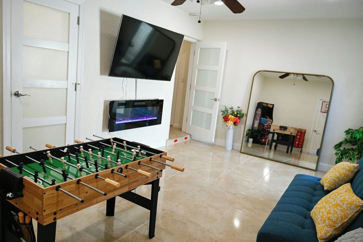 Een kamer met een tafelvoetbalspel, een aan de muur bevestigde televisie en een bank met kussens.