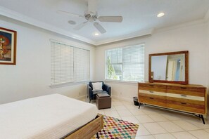 Ein Schlafzimmer mit Bett, Stuhl, Schminktisch, Deckenventilator und einem Fenster mit Jalousien.