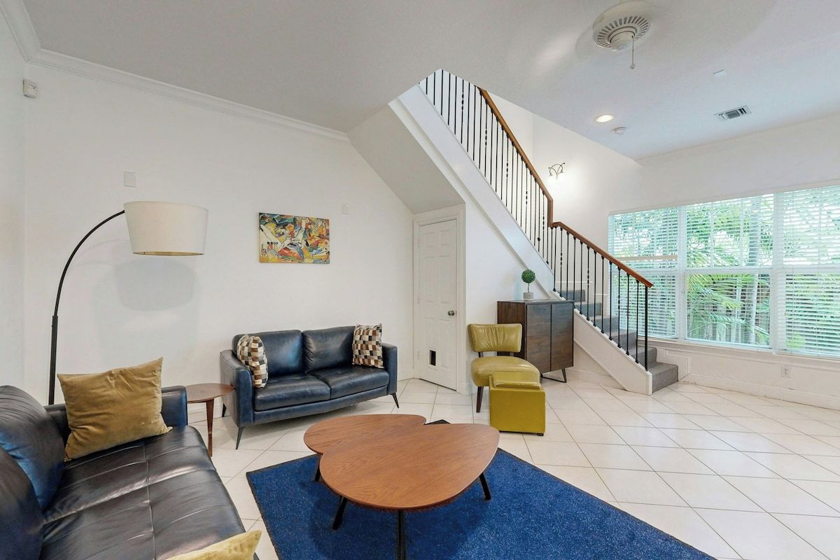 A spacious living room with a staircase, a sofa, a coffee table, and a lamp.