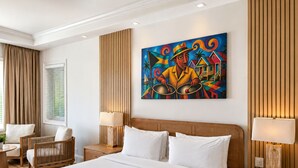 A hotel room with a large bed, two bedside tables, a chair, a window with curtains, and a colorful painting on the wall. - Brookes Guest House (Freeport)