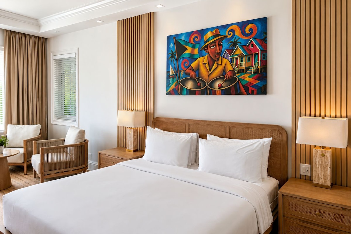 Habitación de hotel con una cama grande, dos mesitas de noche, una silla, una ventana con cortinas y un cuadro llamativo en la pared.