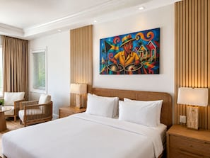 Habitación de hotel con una cama grande, dos mesitas de noche, una silla, una ventana con cortinas y un cuadro llamativo en la pared.