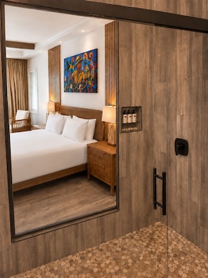 A hotel room with a large bed, a nightstand, a lamp, a painting on the wall, and a mirror reflecting the room.