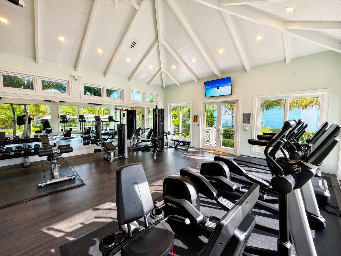 A gym with various exercise equipment, large windows, and a television.
