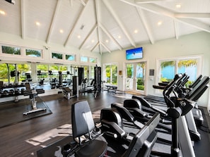 Un gimnasio con diverso equipo de ejercicio, ventanas amplias y una televisión.