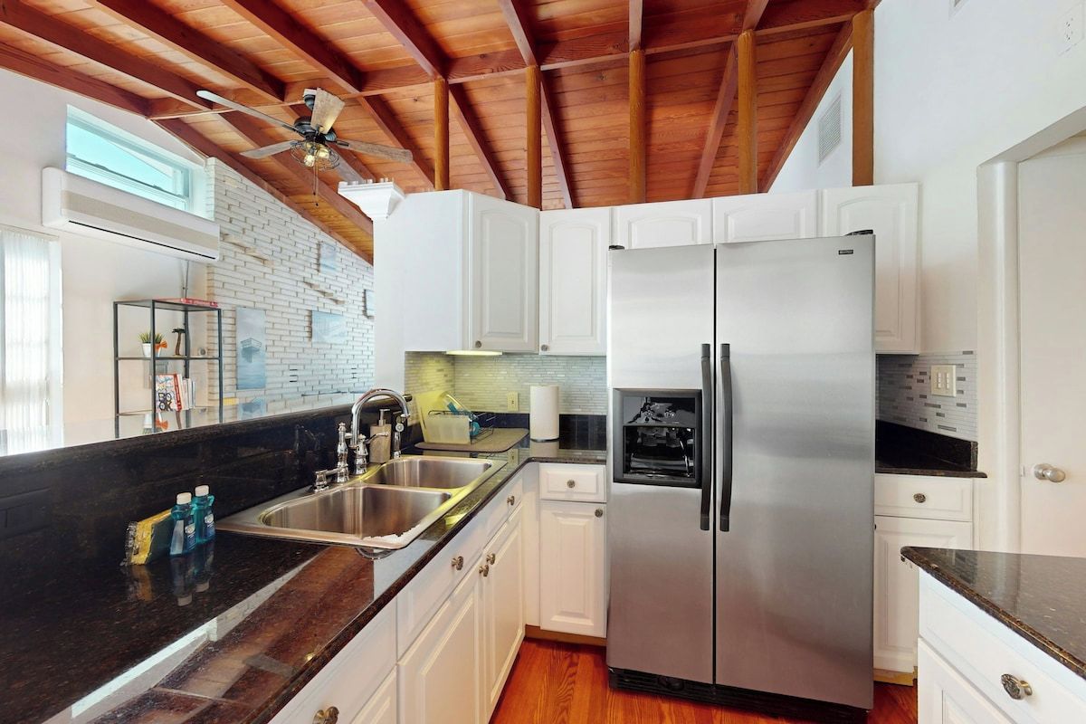 A kitchen with white cabinets, a stainless steel refrigerator, a black countertop, and a wooden ceiling.