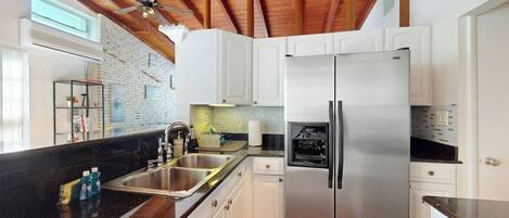 Una cocina con armarios blancos, un refrigerador de acero inoxidable, una encimera negra y un techo de madera.