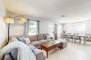 A living room with a sofa, a coffee table, and a dining area with chairs and a table. - Scuba Shack - Enclosed Backyard (West Palm Beach)