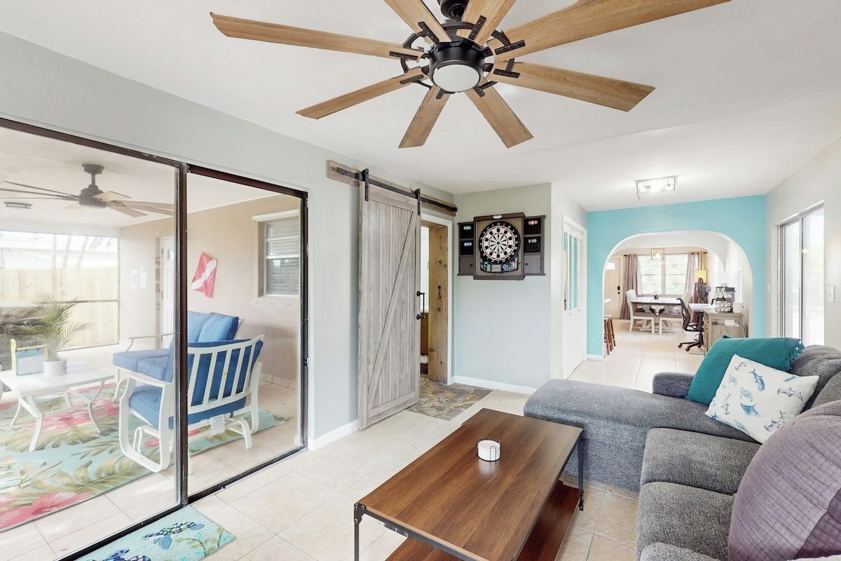 A spacious living room with a ceiling fan, a sliding glass door leading to a patio, and a dining area visible through an archway.