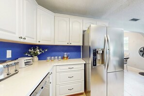 A modern kitchen with white cabinets, a stainless steel refrigerator, a coffee maker, and a toaster. - Scuba Shack - Enclosed Backyard (West Palm Beach)