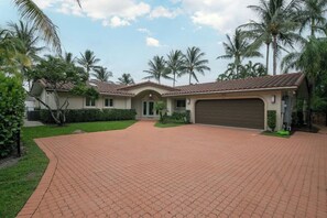 A residential property with a paved driveway, a garage, and palm trees. - Paradise Manor - Private Pool (Pompano Beach)