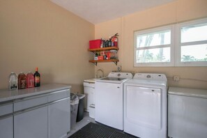 A laundry room with a washing machine, dryer, and shelves with cleaning supplies. - Paradise Manor - Private Pool (Pompano Beach)