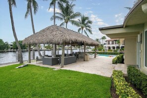 A thatched-roof outdoor seating area with a pool and palm trees. - Paradise Manor - Private Pool (Pompano Beach)