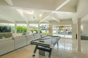A spacious living area with a pool table, a large sofa, and a television. - Paradise Manor - Private Pool (Pompano Beach)