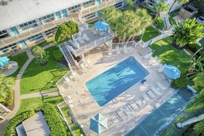 Ein Dachpool mit Liegestühlen und Sonnenschirmen, umgeben von Grünflächen und einem Gebäude mit Balkonen.