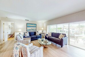 A spacious living room with a large glass coffee table, two sofas, and a view of the outdoors through large windows. - Singer Island Serenity (West Palm Beach)