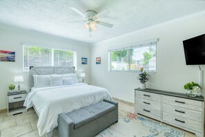Ein Schlafzimmer mit Bett, Nachttischen, einer Bank, einem Schminktisch und Fenstern.