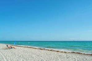A beach with a clear sky, calm sea, and a person lying on a beach towel. - Iconic Views - Luxury Condo in the Heart of Brickell (Miami)