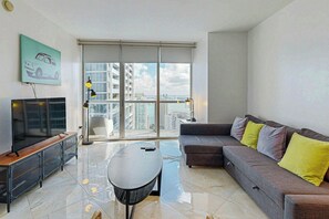 A modern living room with a sofa, a coffee table, a TV, and a large window with a city view. - Iconic Views - Luxury Condo in the Heart of Brickell (Miami)