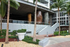 A modern building with large cylindrical columns, a staircase, and a landscaped area with palm trees and a large planter. - Iconic Views - Luxury Condo in the Heart of Brickell (Miami)