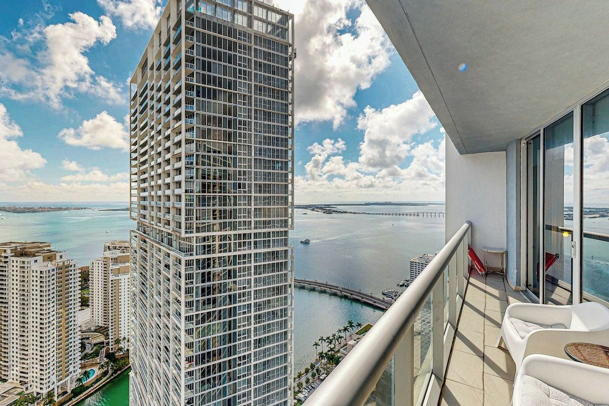 A high-rise building with a balcony overlooking a marina and a bridge.